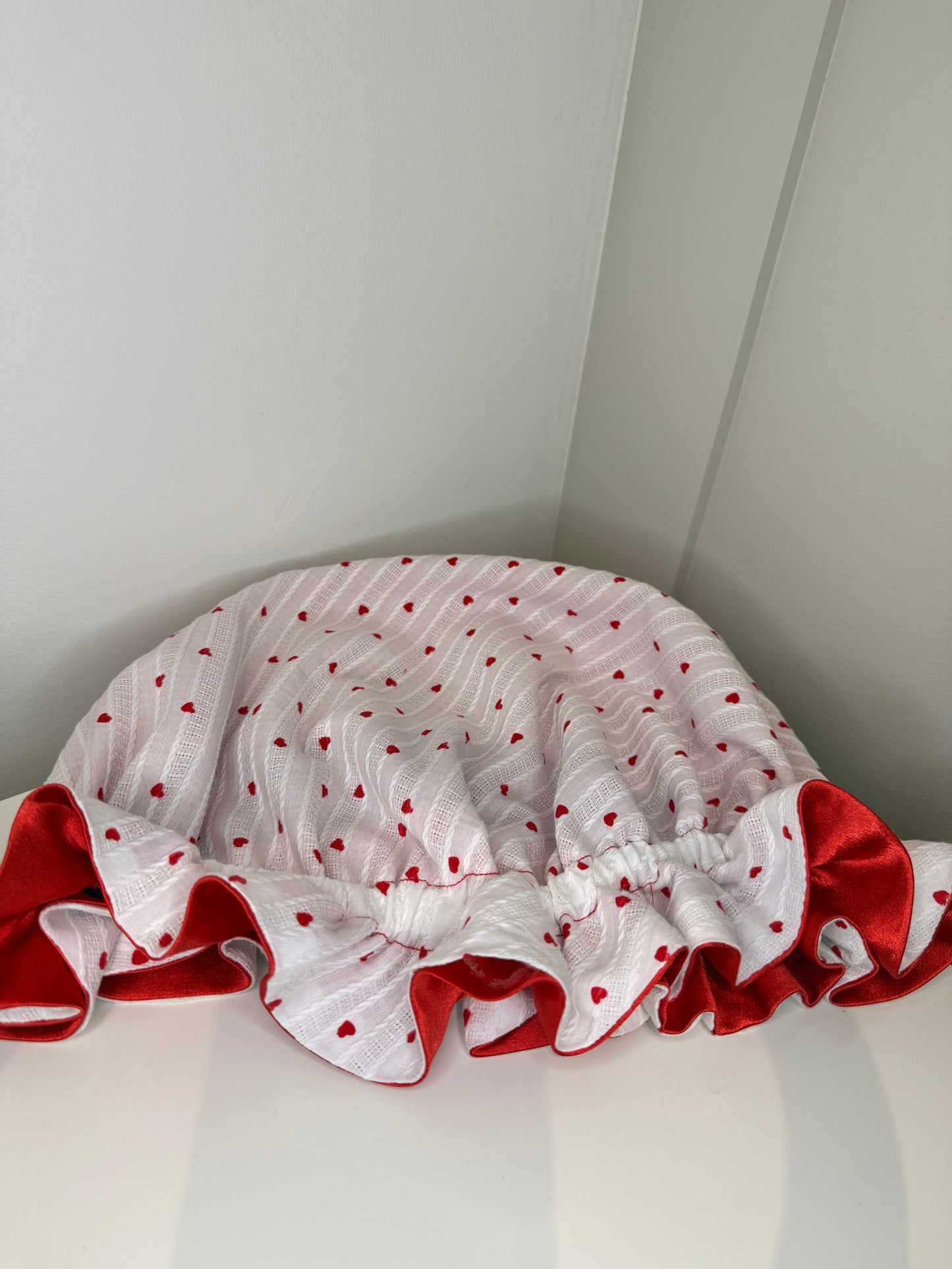 White sleep cap with red heart patterns, with luxurious satin on a white surface.