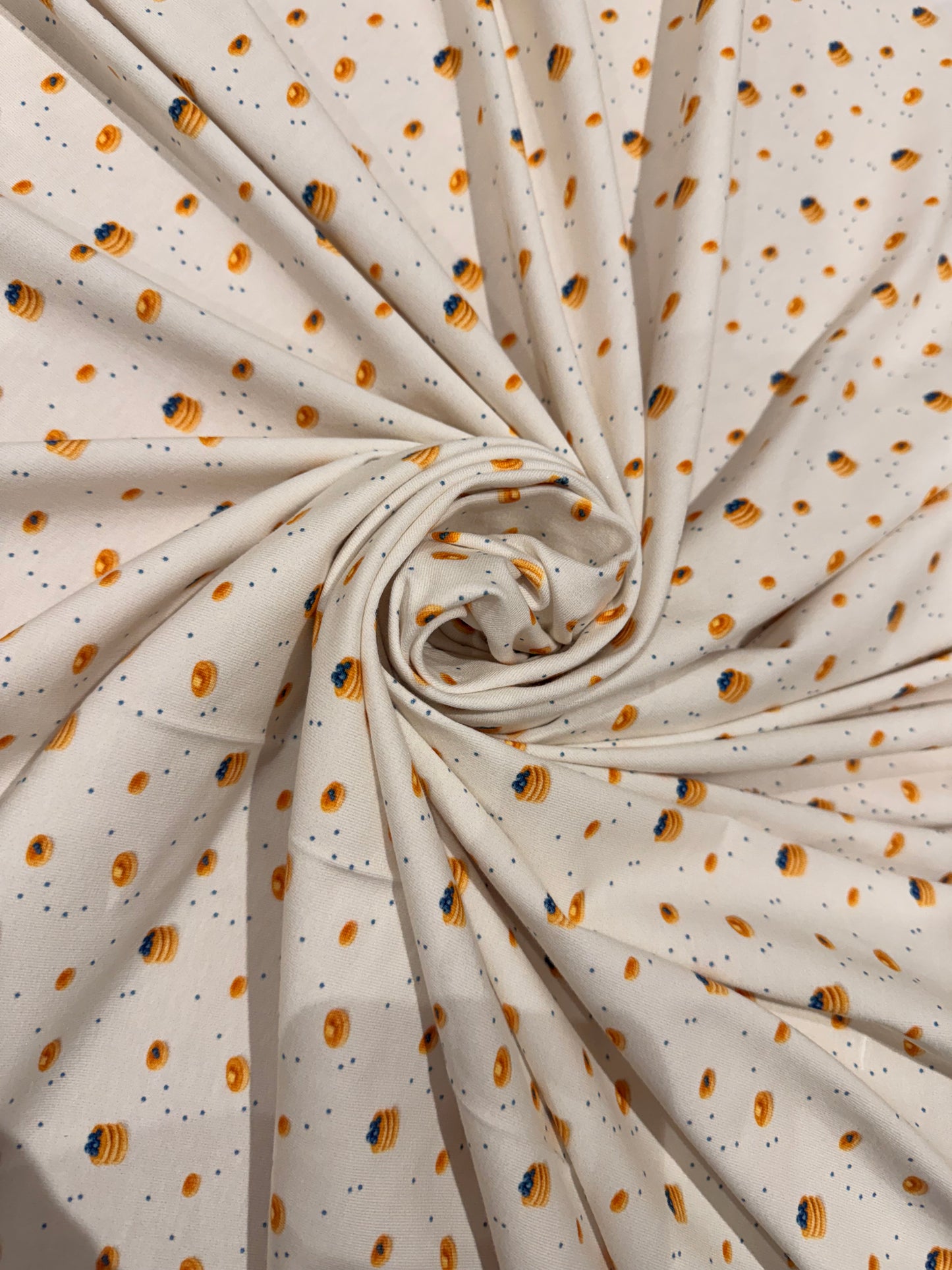 Rolled-up fabric with a pattern of small dots and little pancakes and blueberry pancake stacks on a beige background