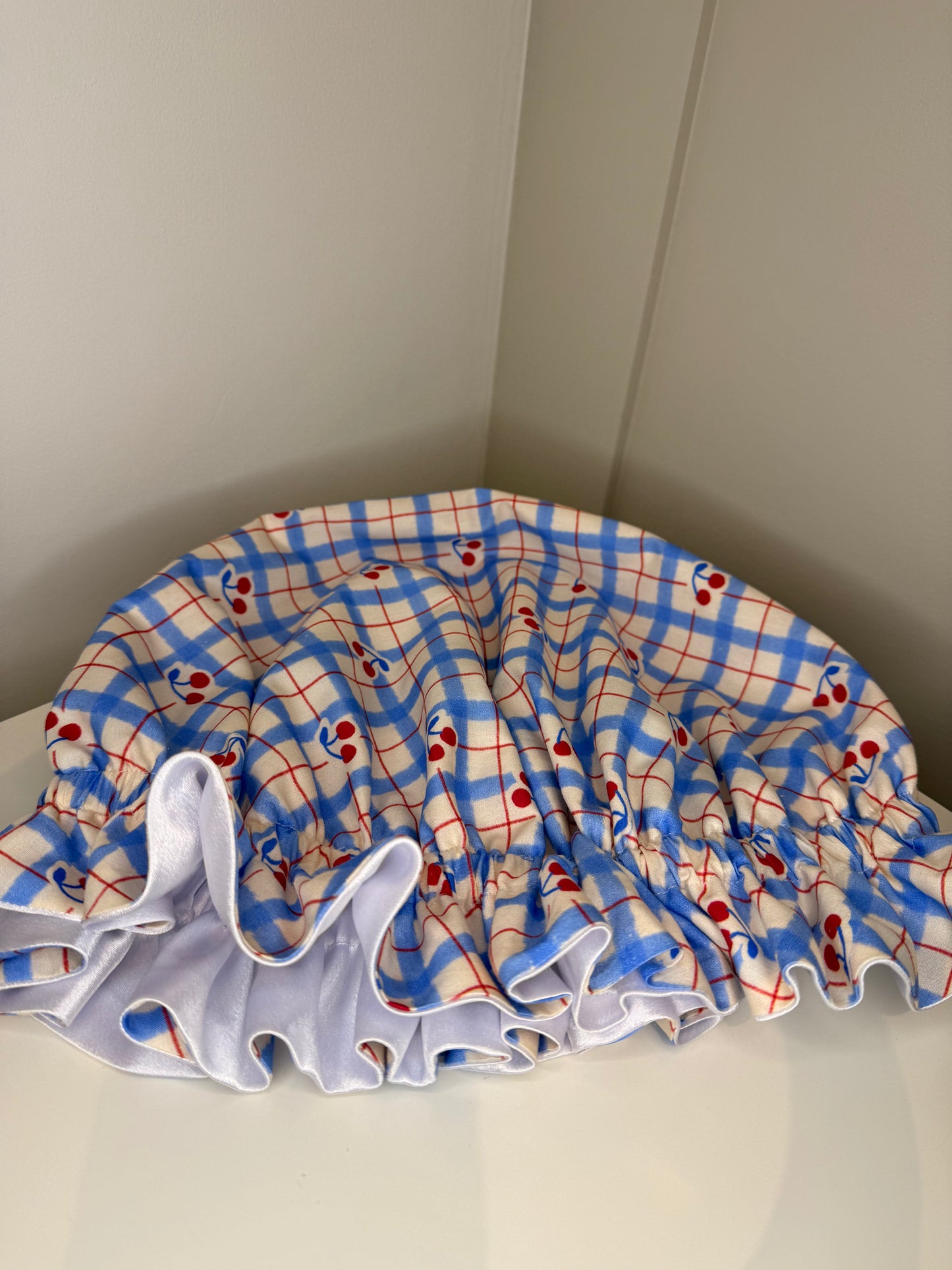 Plaid-patterned with cherries sleep cap on a white surface with a neutral background