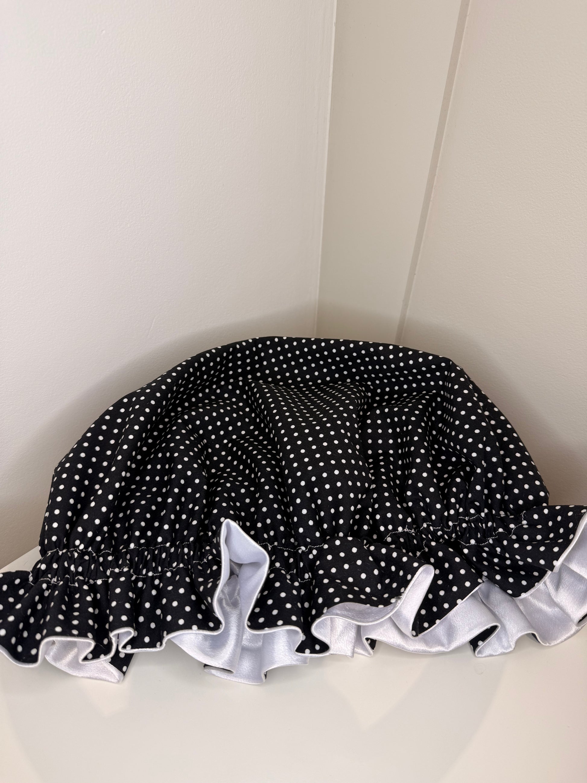Black and white polka dot bonnet closed with white ruffle on a white background