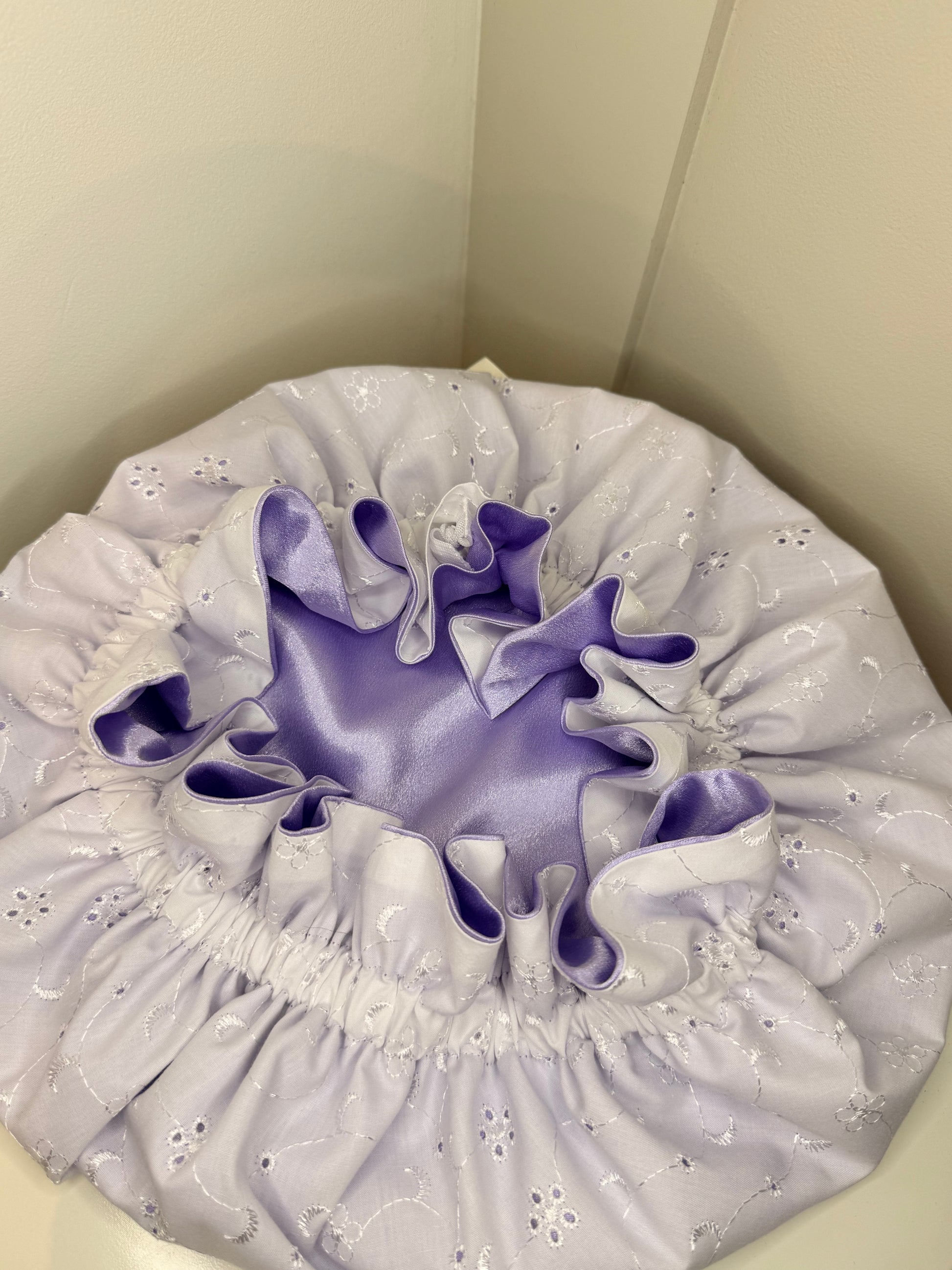 Decorative bonnet with white anglaise and purple satin on a neutral background