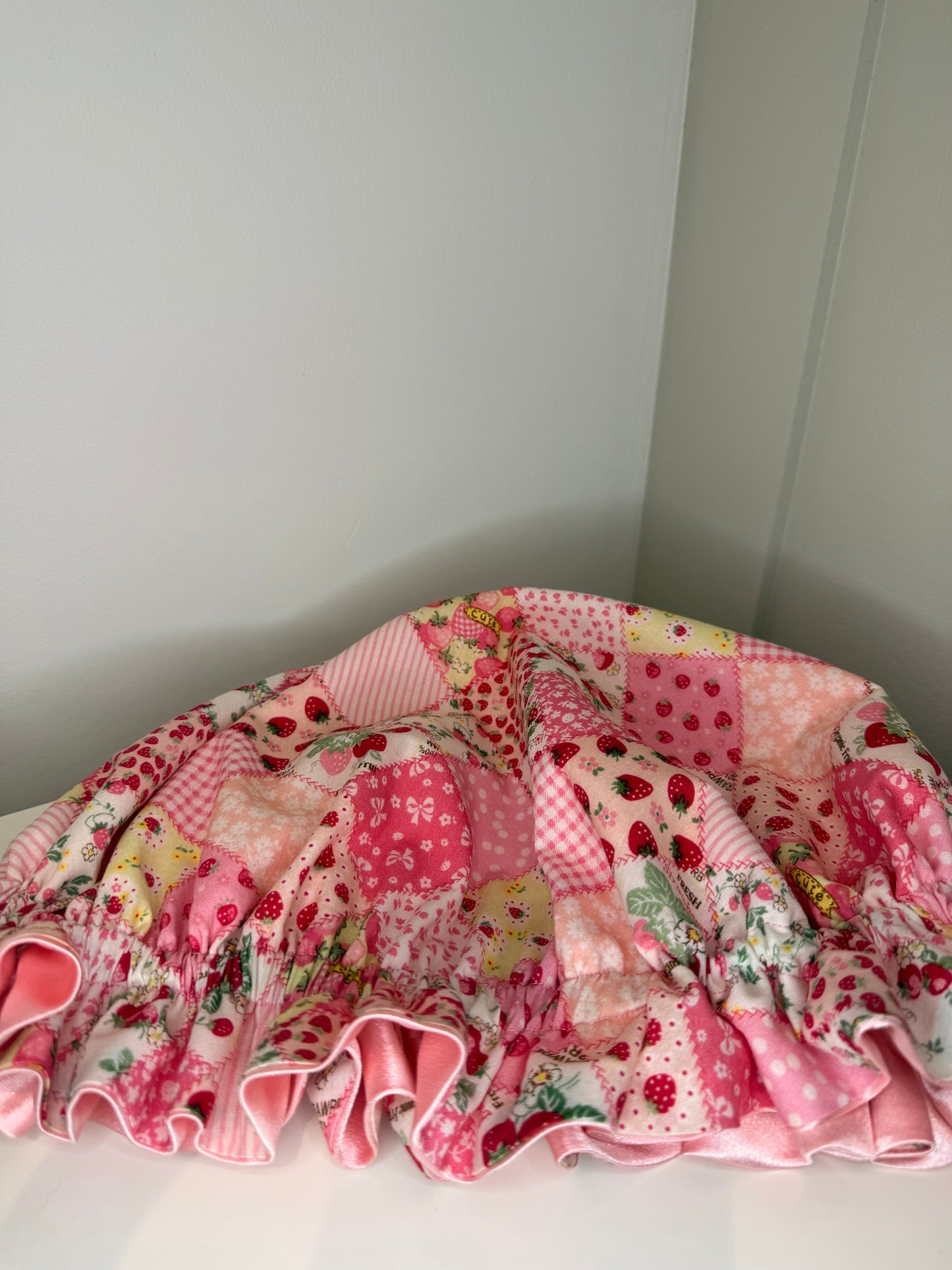 Adjustable satin bonnet with strawberry design patchwork fabric, on a white surface.