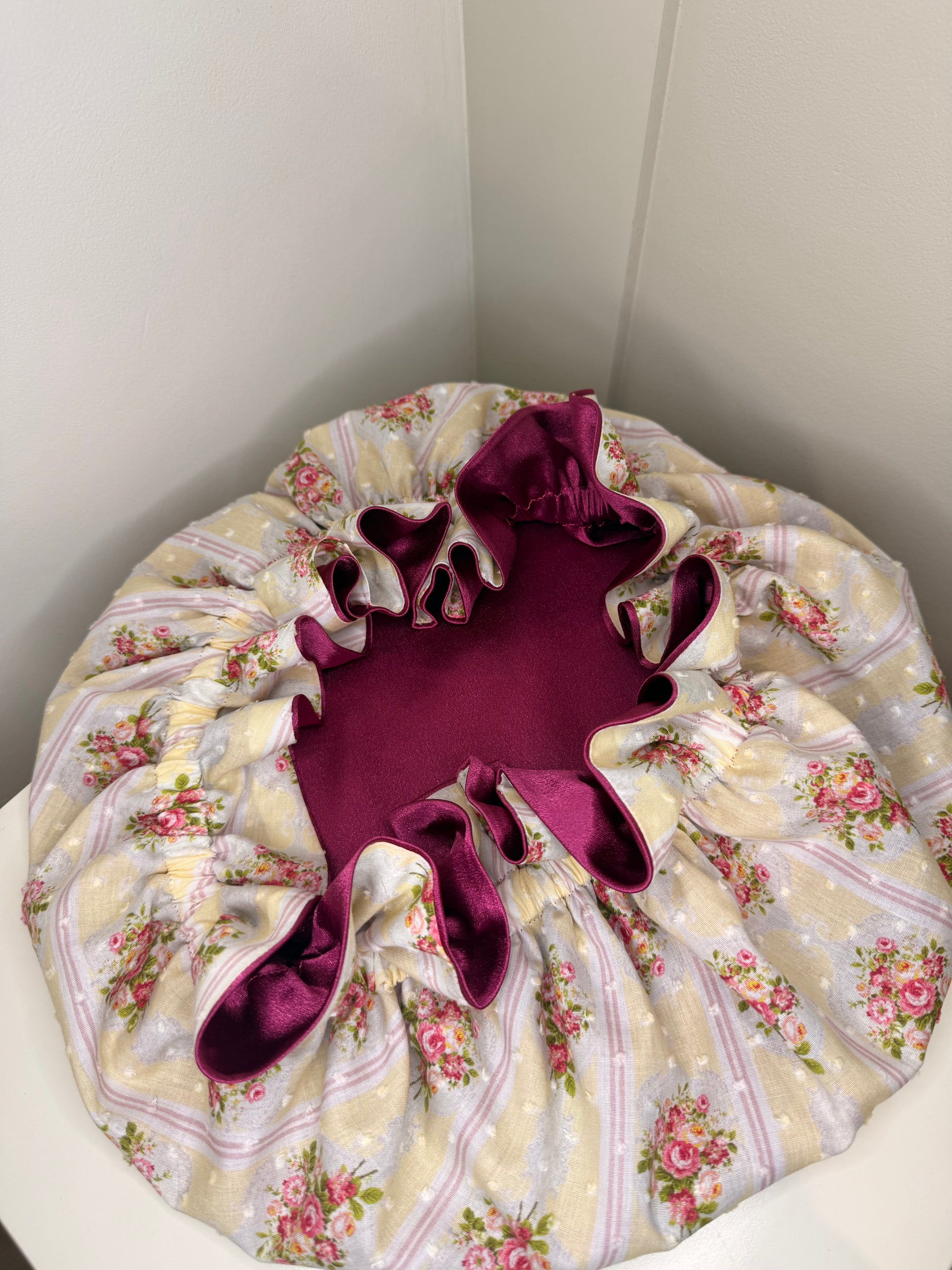 Floral-patterned bonnet with a purple satin showing inside on a white surface