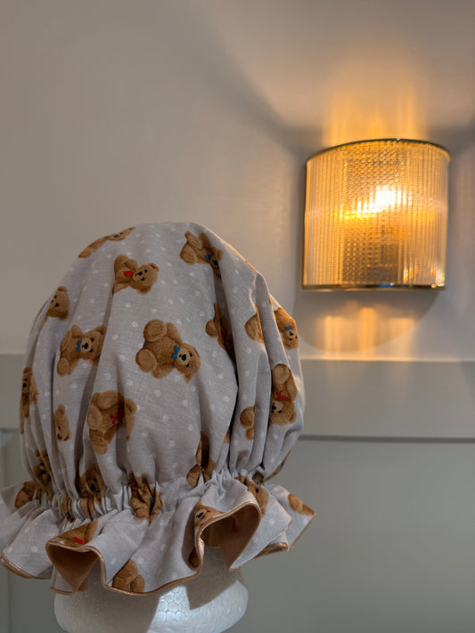 Mannequin wearing a satin bonnet with teddy bear pattern in a room with a lamp.