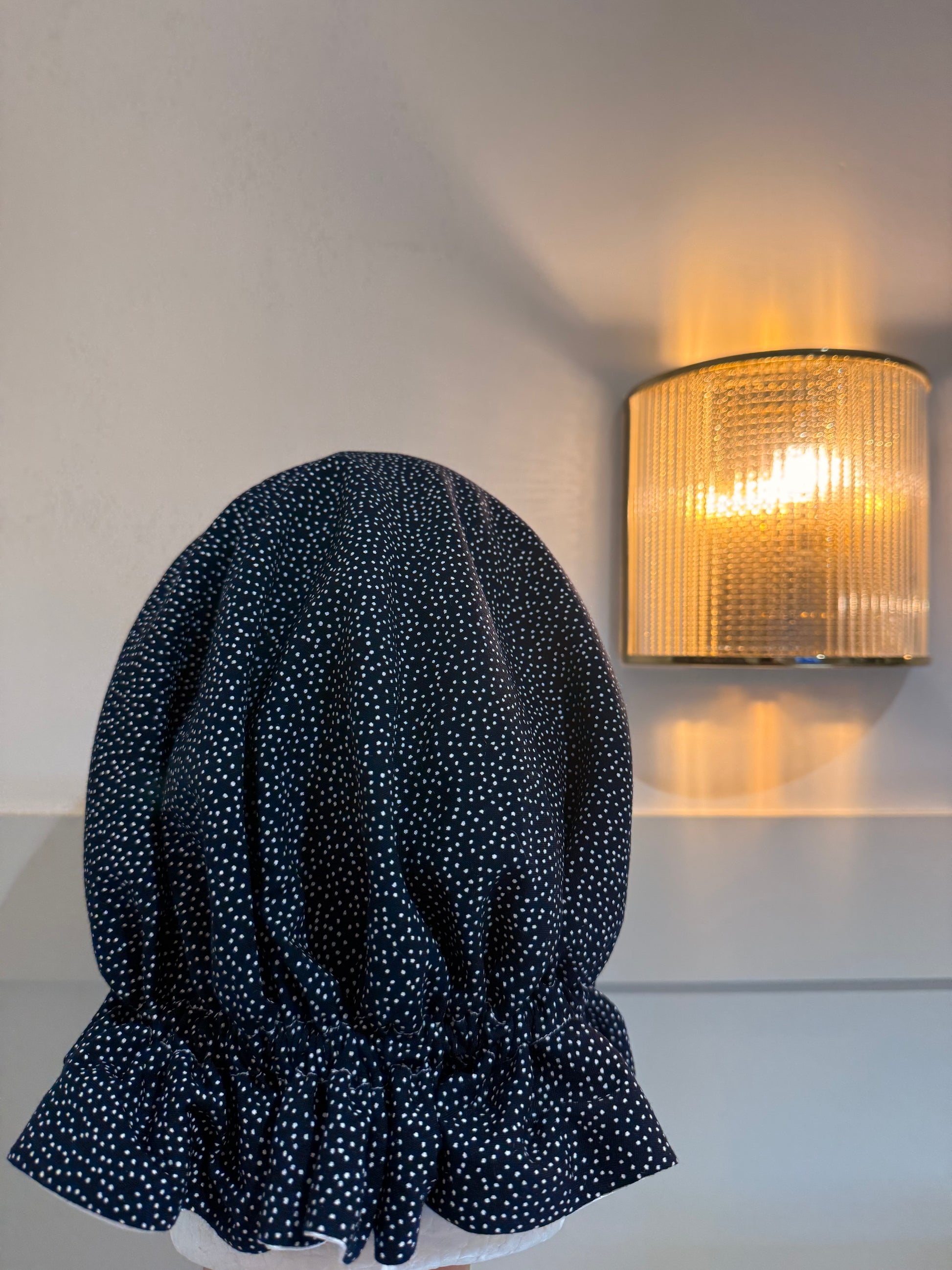 A navy blue adjustable bonnet with small white polka dots, with white satin 