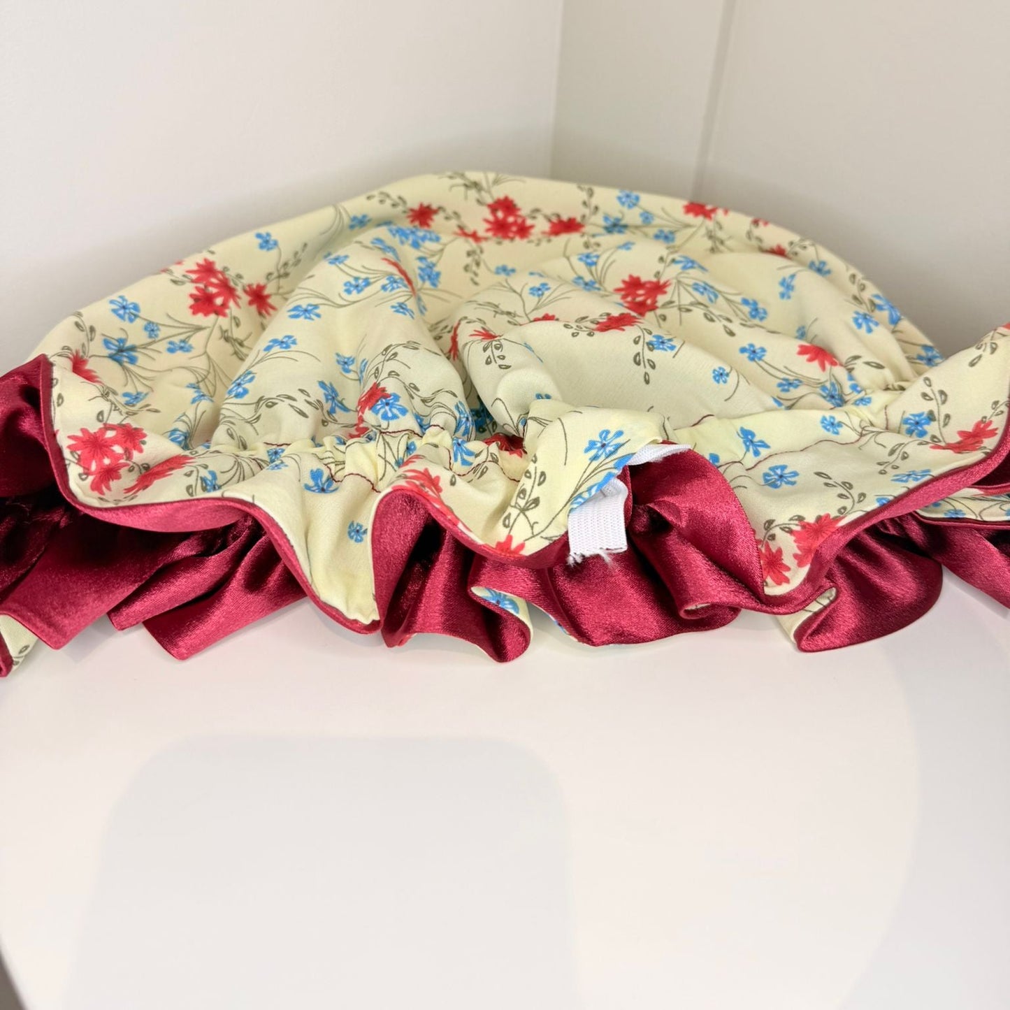 Floral-patterned red and blue bonnet on cream crepe material with red satin on a white background