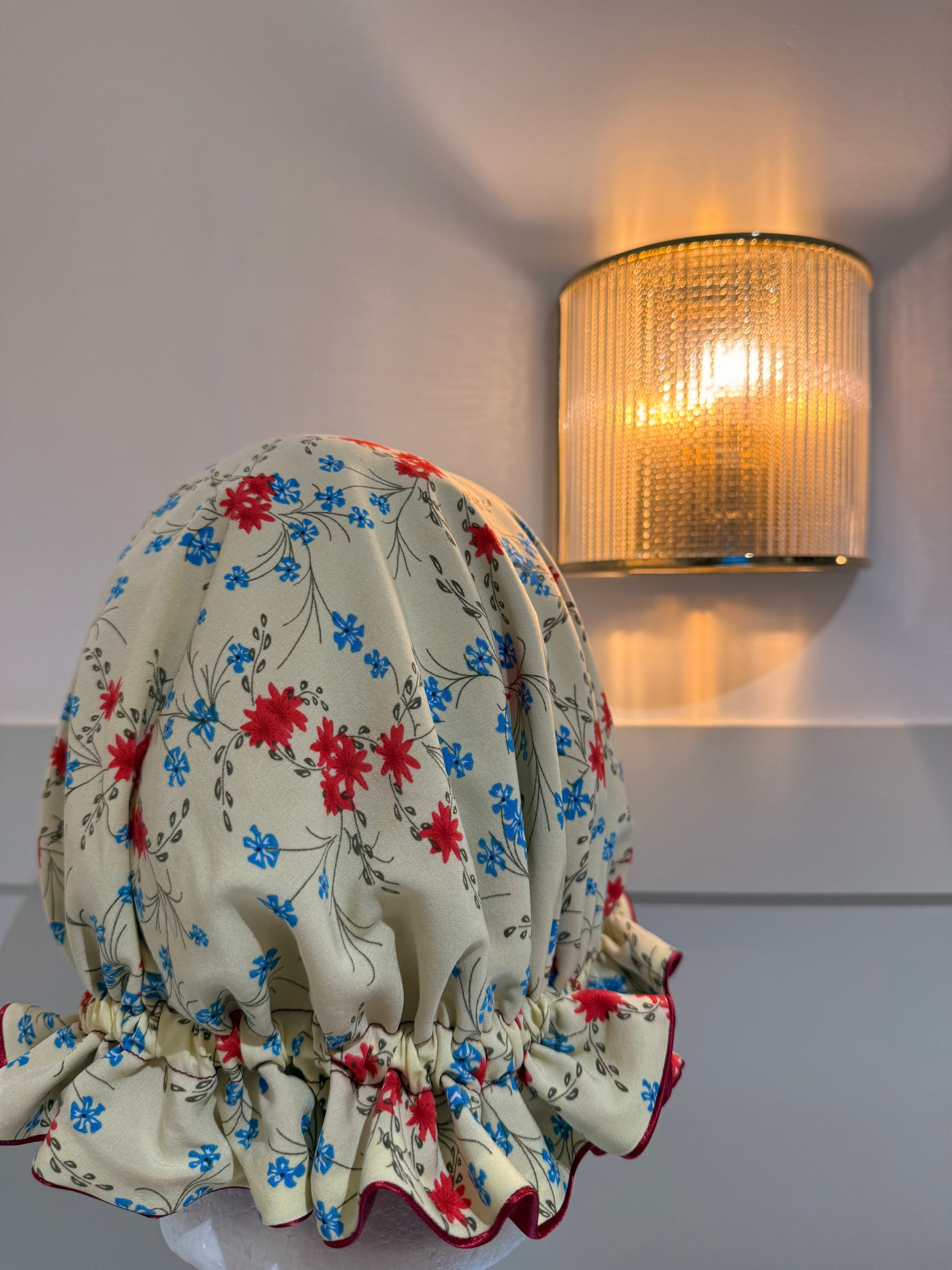 Floral-patterned sleep cap on a white surface with a wall-mounted light fixture in the background. Made in the UK.