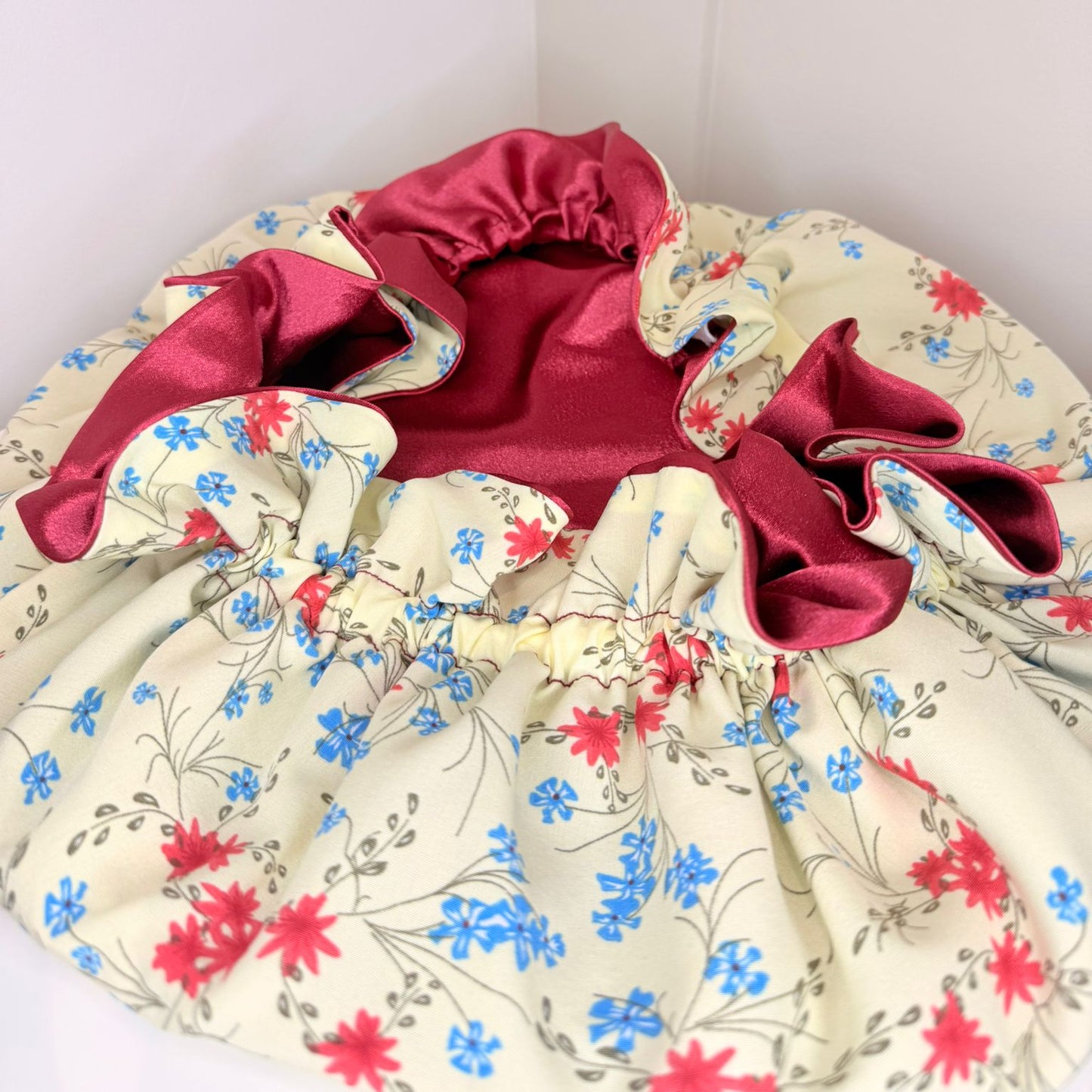 Floral-patterned bonnet with red trim on a white background. 