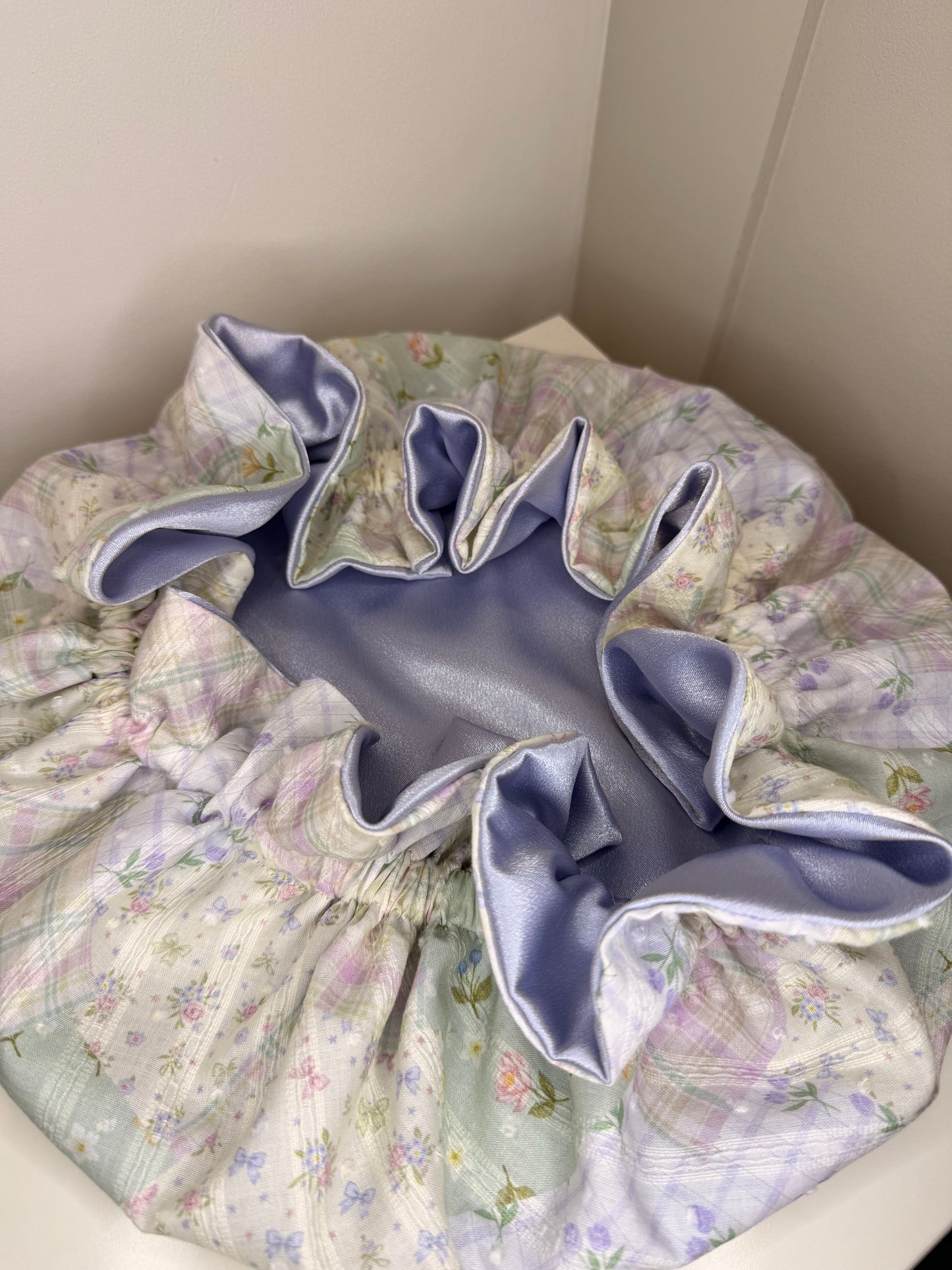 Floral-patterned, striped pastel bonnet with ruffled edge on a plain background