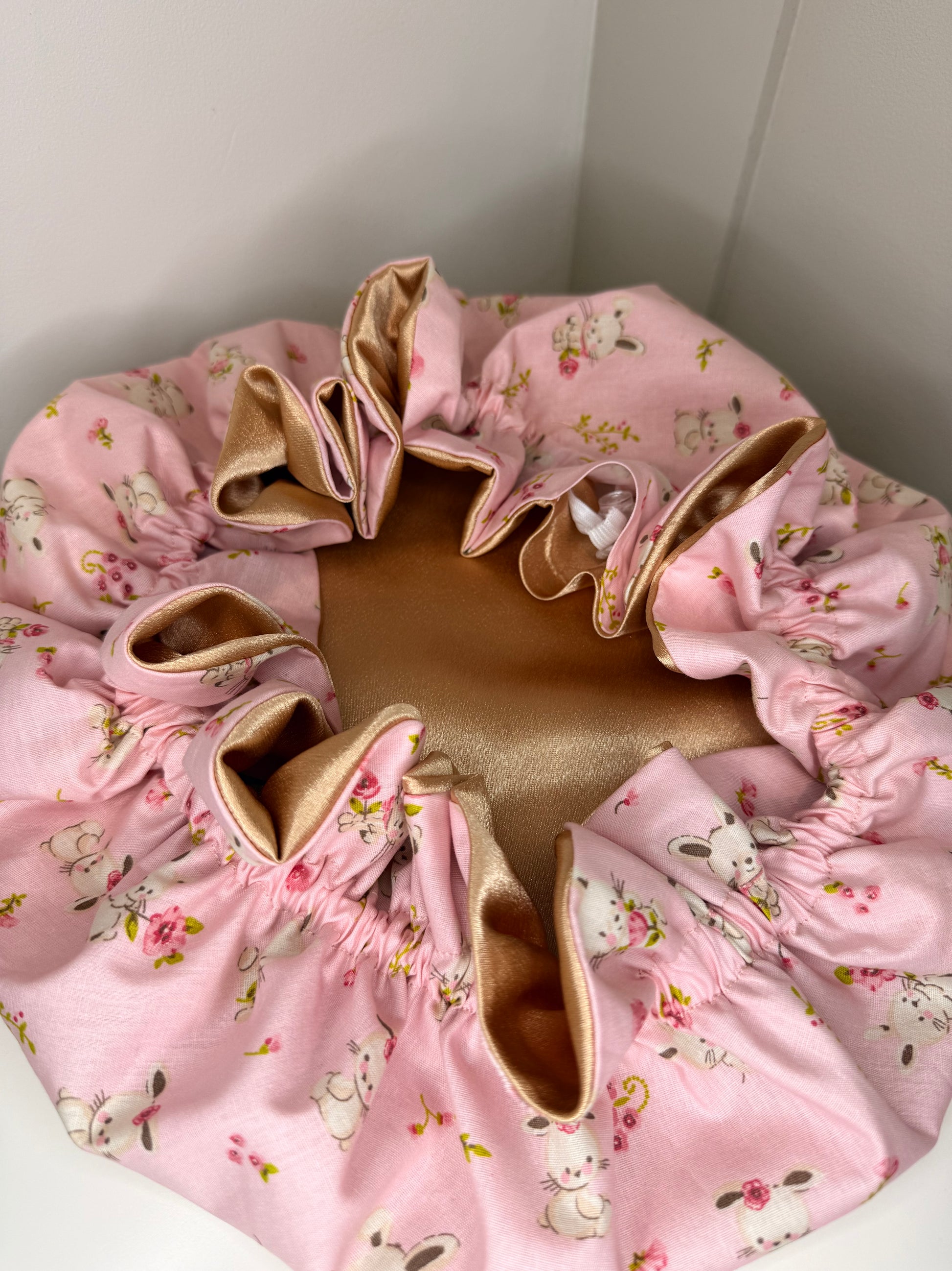 Pink floral-patterned and bunny designed satin bonnet on a white surface. Sold in the UK and EU.