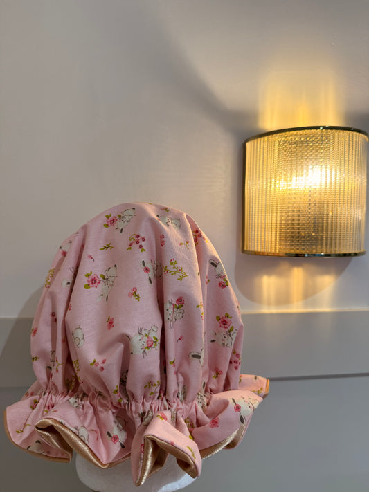 Pink floral-patterned sleep cap on a white surface with a light fixture in the background. Made in the UK.