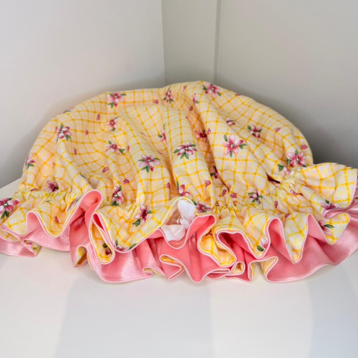 Yellow lattice and pink floral-patterned satin bonnet on a white surface