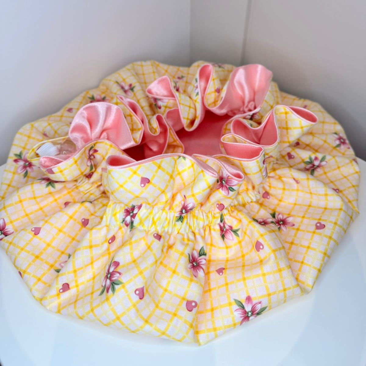 Yellow floral-patterned bonnet with pink satin lining on a white background