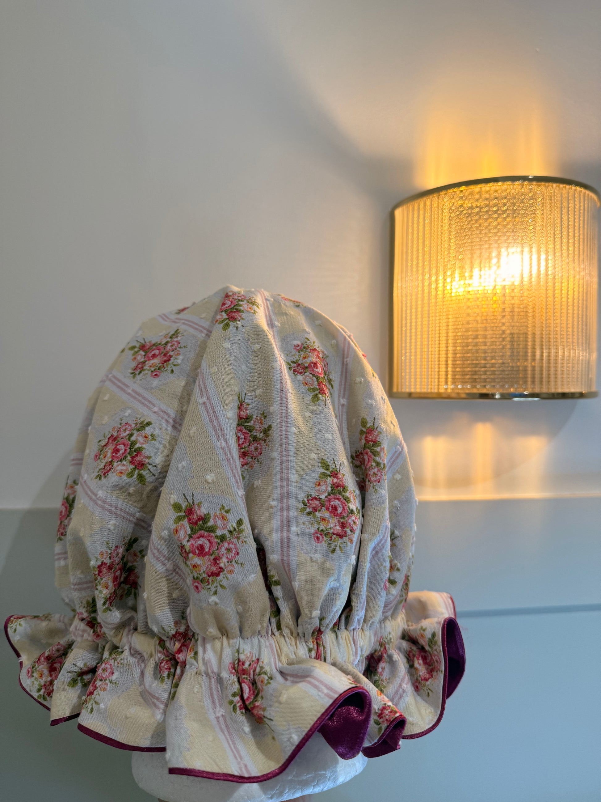 Floral-patterned satin sleep cap on a white surface with a lamp in the background