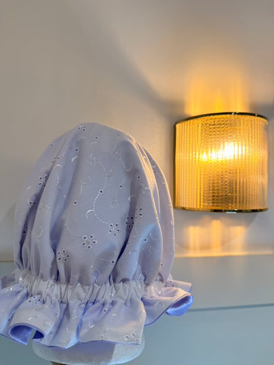 Light purple embroidered bonnet on a white surface with a warm light fixture in the background.