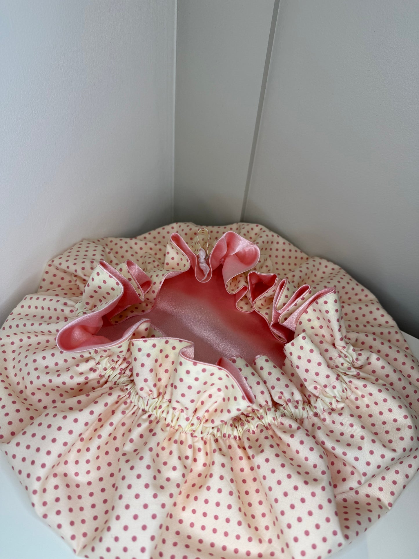 Pink and white polka dot fabric-covered bonnet, with pink luxury satin, on a white surface