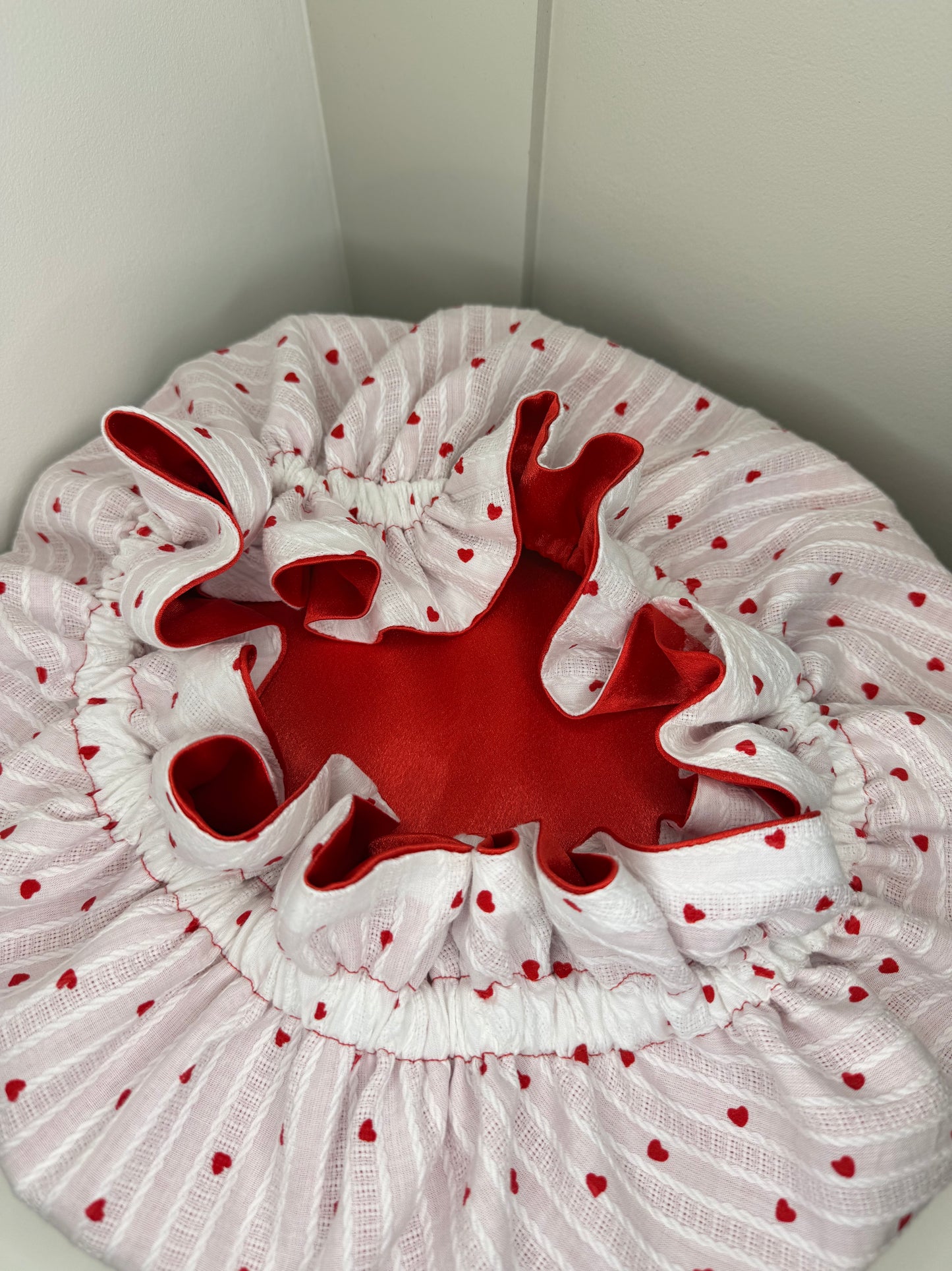 White bonnet with red hearts pattern, and a red satin interior, on a white background