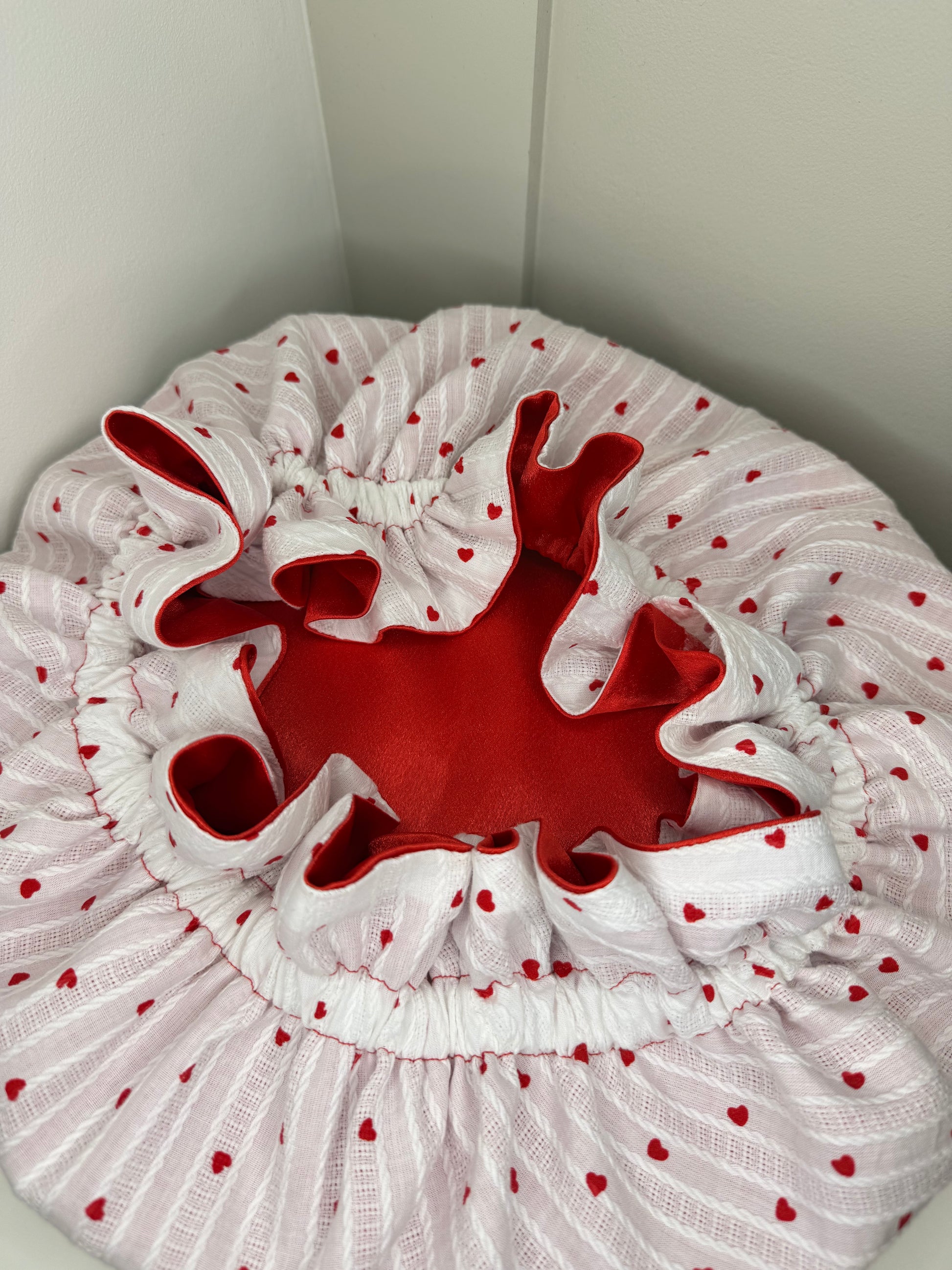 White bonnet with red hearts pattern, and a red satin interior, on a white background