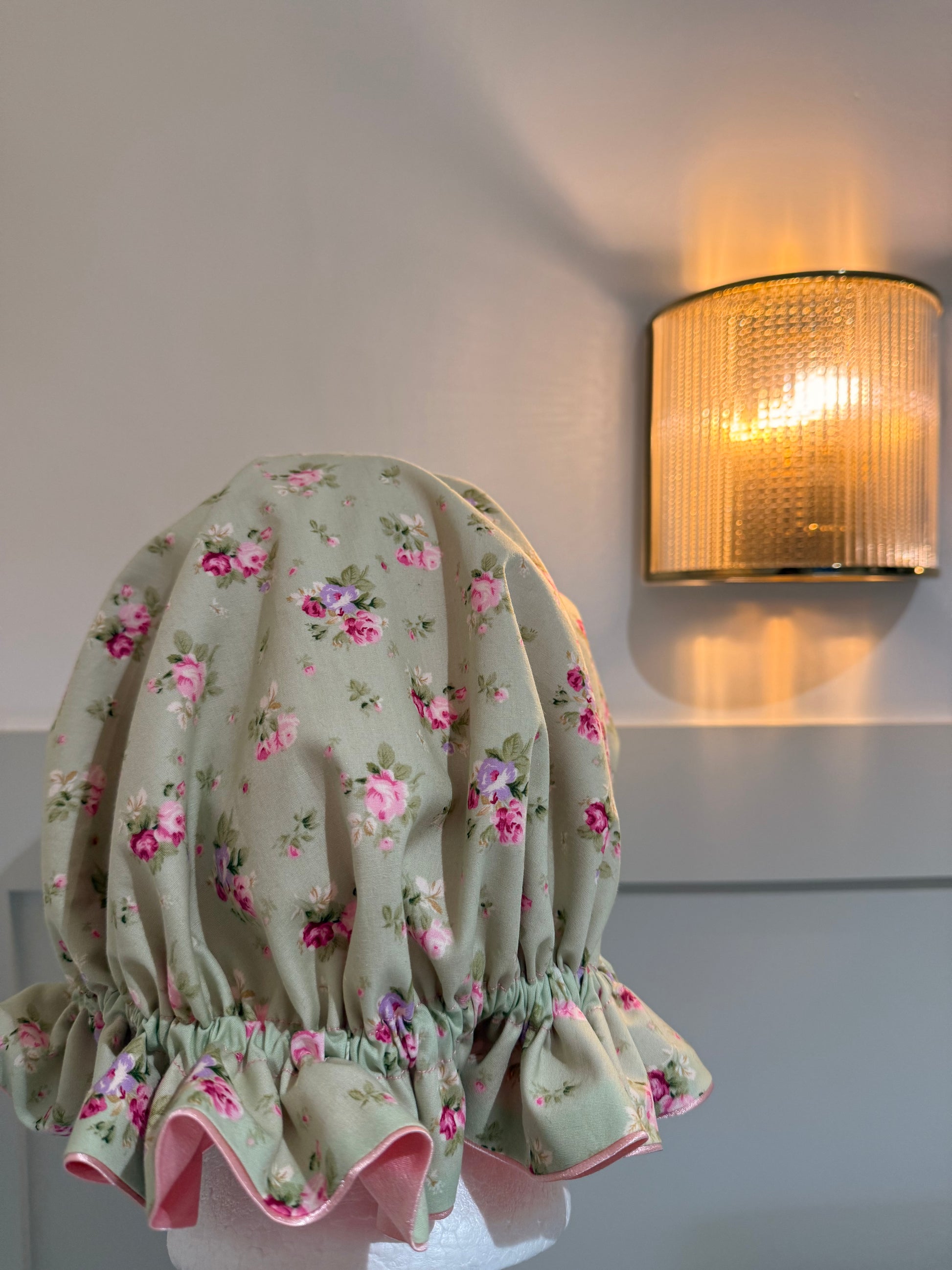 A pink satin bonnet with green fabric on top with an array of blossoming roses 