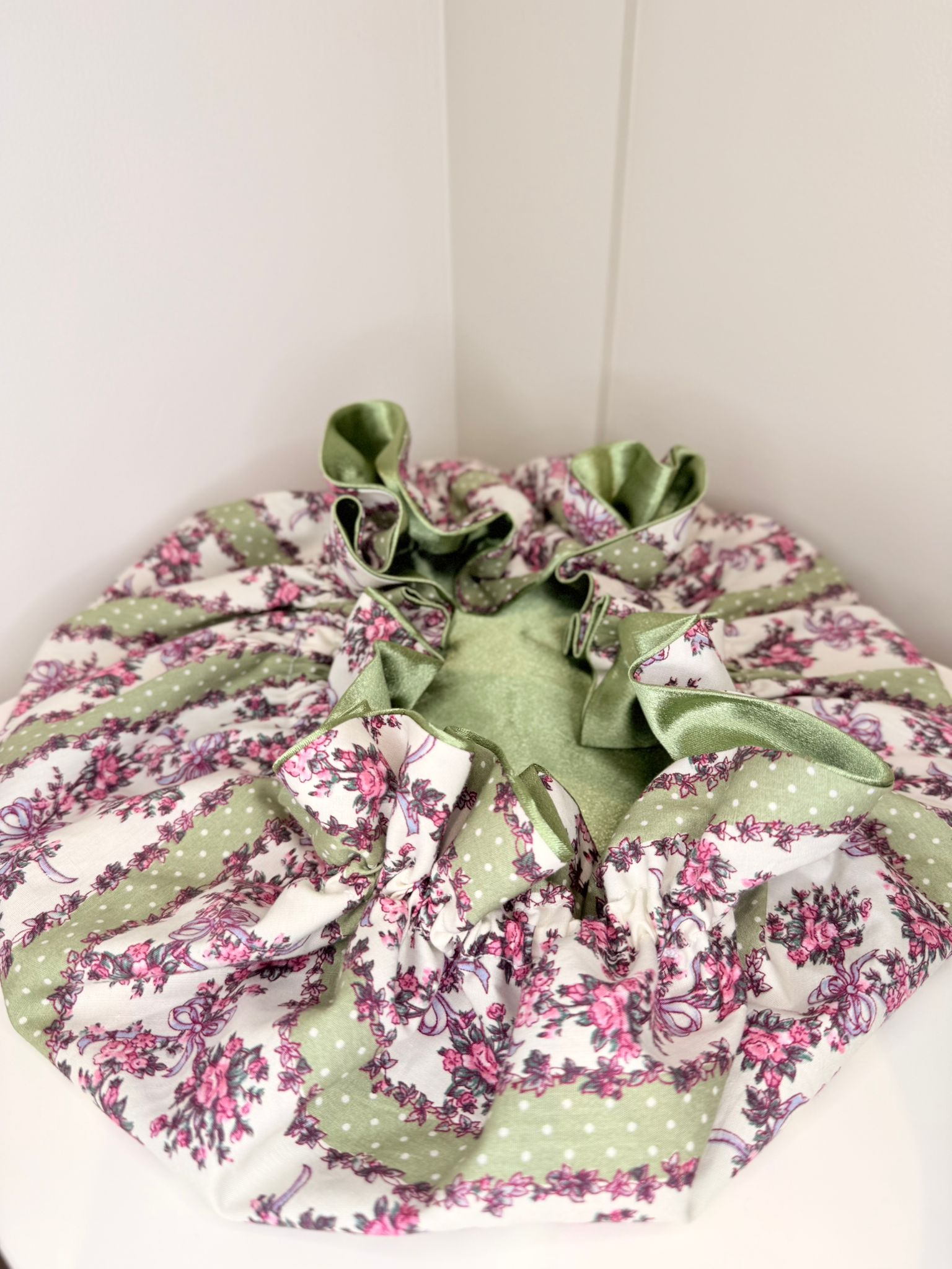 Floral fabric drawstring bonnet with green satin, showing adjustable toggle, on a white background. made in the uk.