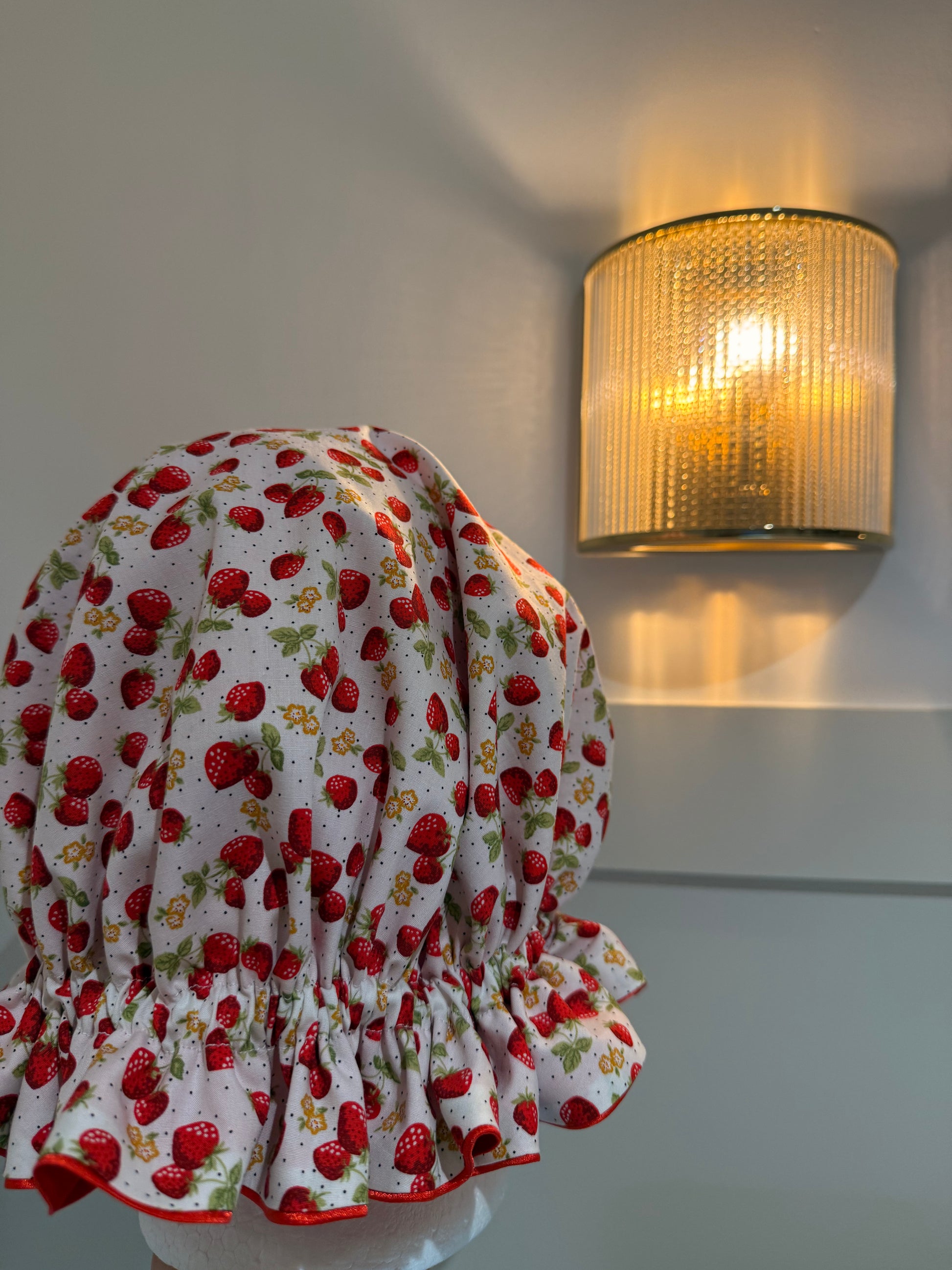 Red and white floral strawberry print satin bonnet  on a mannequin with a wall-mounted light fixture in the background.