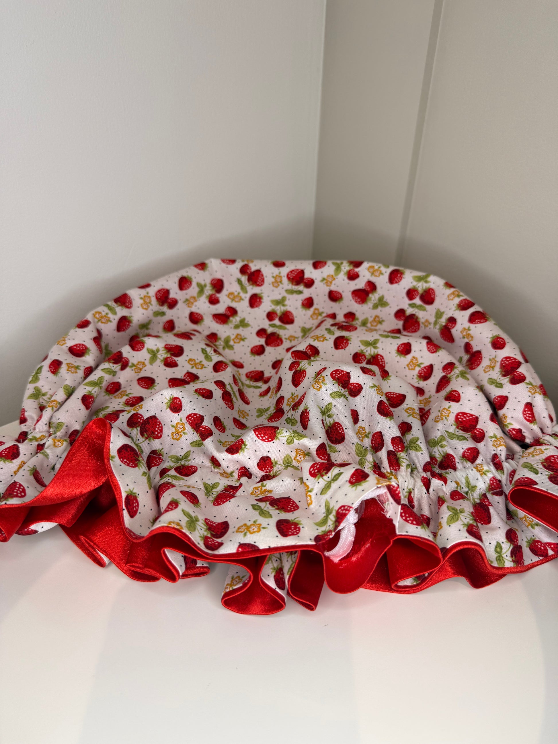 Satin bonnet with strawberry pattern on a white surface showing ajustabke drawstring 