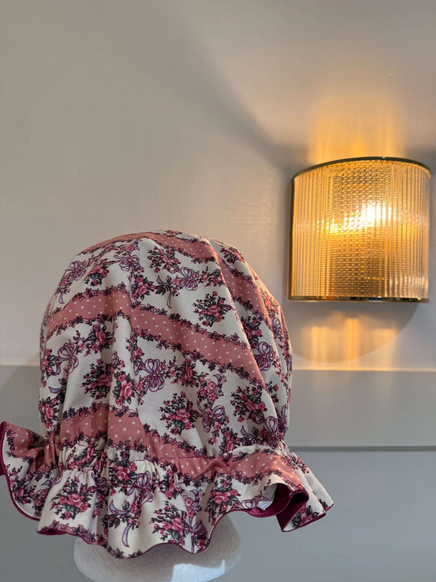 Floral-patterned bonnet on a white surface with a wall-mounted light fixture in the background.